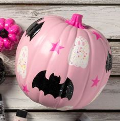 a pink painted pumpkin with bats and stars on it sitting next to other halloween decorations