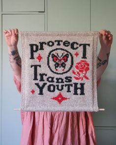 a woman holding up a cross - stitched sign that says protect those yoth