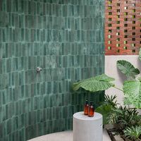 a bathroom with green tiles on the wall and plants in the bathtub next to it