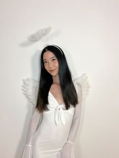 a woman with long black hair wearing a white dress and angel wings on her head