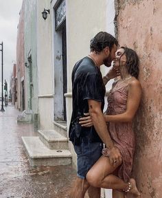 a man and woman standing next to each other in the rain, kissing with one another