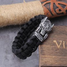 a black bracelet with a silver skull on it next to a wooden box and rope