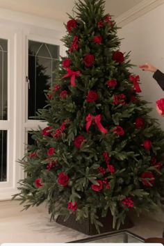 a woman standing in front of a christmas tree with red roses on it's branches