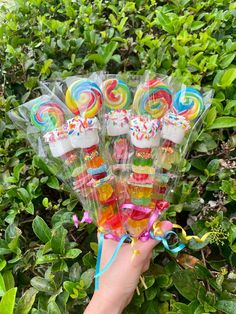 a hand holding candy lollipops in front of some bushes