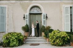 a bride and groom standing in front of a door with shutters on each side