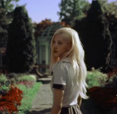 a blonde haired girl with long white hair standing in front of flowers and trees, looking at the camera