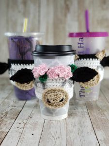 three coffee cups with crocheted animals on them, one is holding a cup and the other has a straw in it