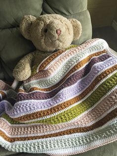 a brown teddy bear sitting on top of a couch under a crocheted blanket