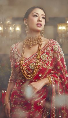 a woman in a red and gold dress with jewelry on her neck, standing next to a mirror