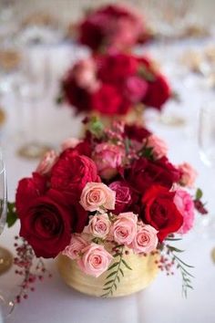 red and pink flowers in a gold vase on a white table cloth with silverware