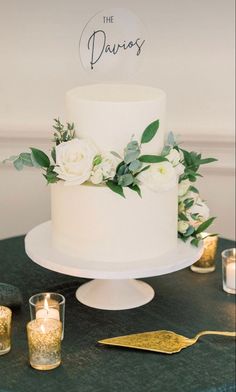 a white wedding cake sitting on top of a table next to candles and greenery