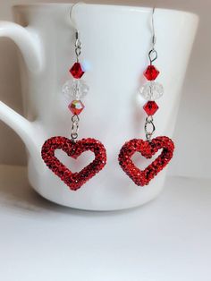 a pair of red heart shaped earrings sitting on top of a white cup