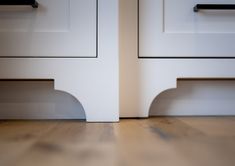 two white drawers with black handles on top of each drawer and wood flooring in front of them