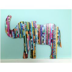 an elephant made out of strips of colored paper on a blue wall next to a white shelf