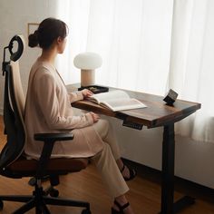 a woman sitting at a desk with a book in front of her, looking out the window