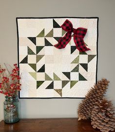 a quilted wall hanging on the wall next to pine cones and a vase filled with flowers