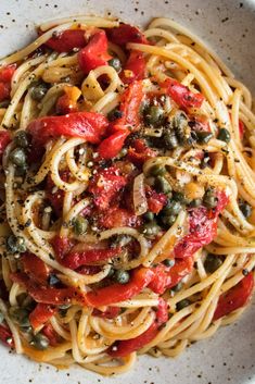 a white bowl filled with pasta, olives and tomatoes on top of a table