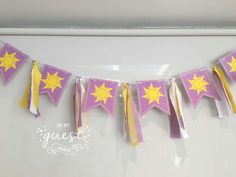 a purple and yellow bunting with sun decorations on the top is hanging in front of a white wall