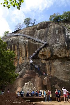 many people are standing at the base of a cliff with a staircase going up it