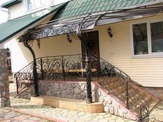 a house with stone steps and wrought iron railings on the front porch, along with a green roof