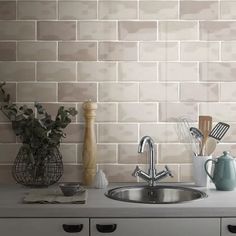 a kitchen sink and counter with utensils on the counter top in front of a brick wall