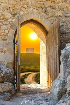 an open door leading to a stone building with a sunset in the background and a dirt path going through it