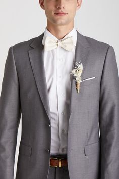 a man wearing a gray suit with a white flower on the lapel and brown belt