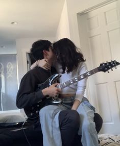 a young man and woman kissing while holding an electric guitar