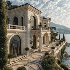 a large white house sitting on top of a hill next to the ocean and trees