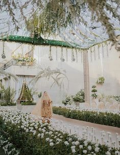 the bride is walking down the aisle with her veil draped over her head, surrounded by white flowers and greenery