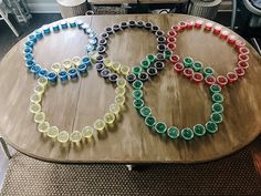 two olympic rings made out of plastic cups on top of a wooden table with chairs in the background