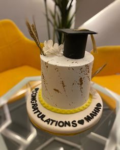 a cake with a graduation hat on top and congratulationss written on the side, sitting in front of a yellow chair