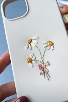 a hand holding a white phone case with flowers on the front and back cover, while it is being held by someone's hand