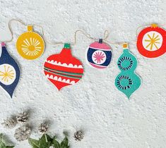 christmas ornaments are hanging on a line against a white wall with flowers in the foreground