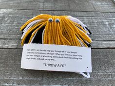 a ball of yarn with eyes on it sitting on top of a wooden floor next to a sign