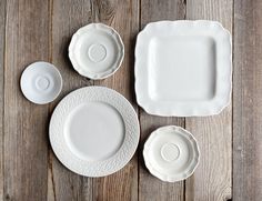 three white plates and two cups on a wooden table with one empty plate in the middle