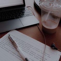 an open notebook and pen on a wooden table next to a laptop computer with a cup of coffee in the background