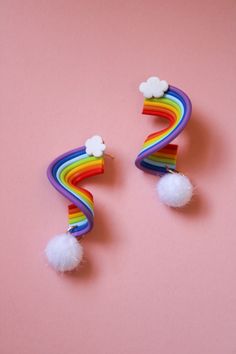 two rainbow earrings with white pom - poms on top of a pink background