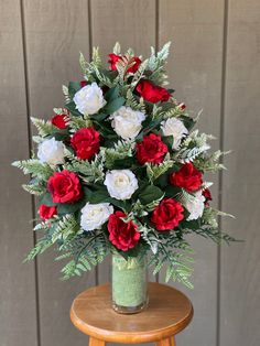 a bouquet of red and white flowers in a green vase on a small wooden table