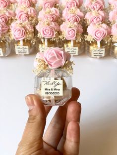 a hand holding a small bottle with pink roses in it next to many smaller bottles