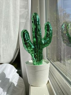 a green cactus sitting on top of a white pot next to a window sill