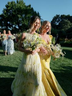 two women in yellow dresses standing next to each other holding bouquets and smiling at the camera