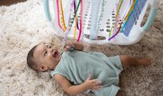 a baby laying on the floor playing with a toothbrush in front of a toy crib