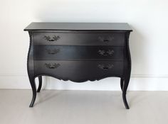 a black chest of drawers sitting on top of a hard wood floor next to a white wall