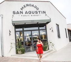 a woman in a red dress is talking on her cell phone while walking past a market