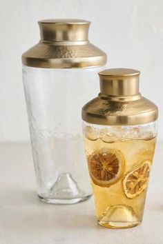 two glass vases with lemon slices in them and one has a gold lid on it