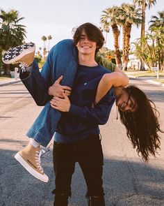 a man carrying a woman on his back while walking down the street with palm trees in the background