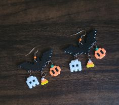 three halloween themed earrings on top of a wooden table with bats and pumpkins hanging from them