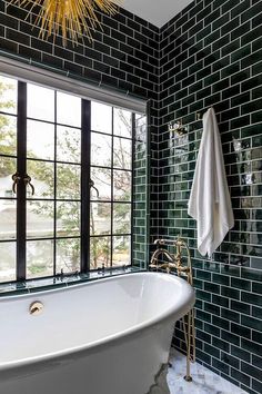 a white bath tub sitting under a window next to a sink in a room with green tile