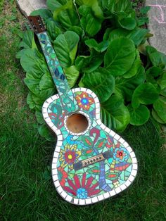 a colorful guitar sitting in the grass next to some plants